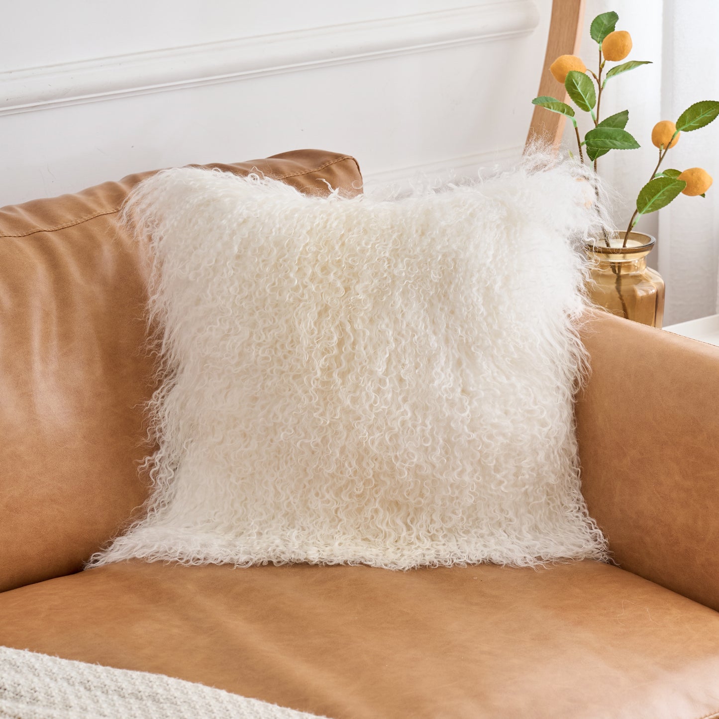 Close-up view of Mongolian lamb fur pillow in natural white on sofa showing soft fluffy curly wool texture in modern interior
