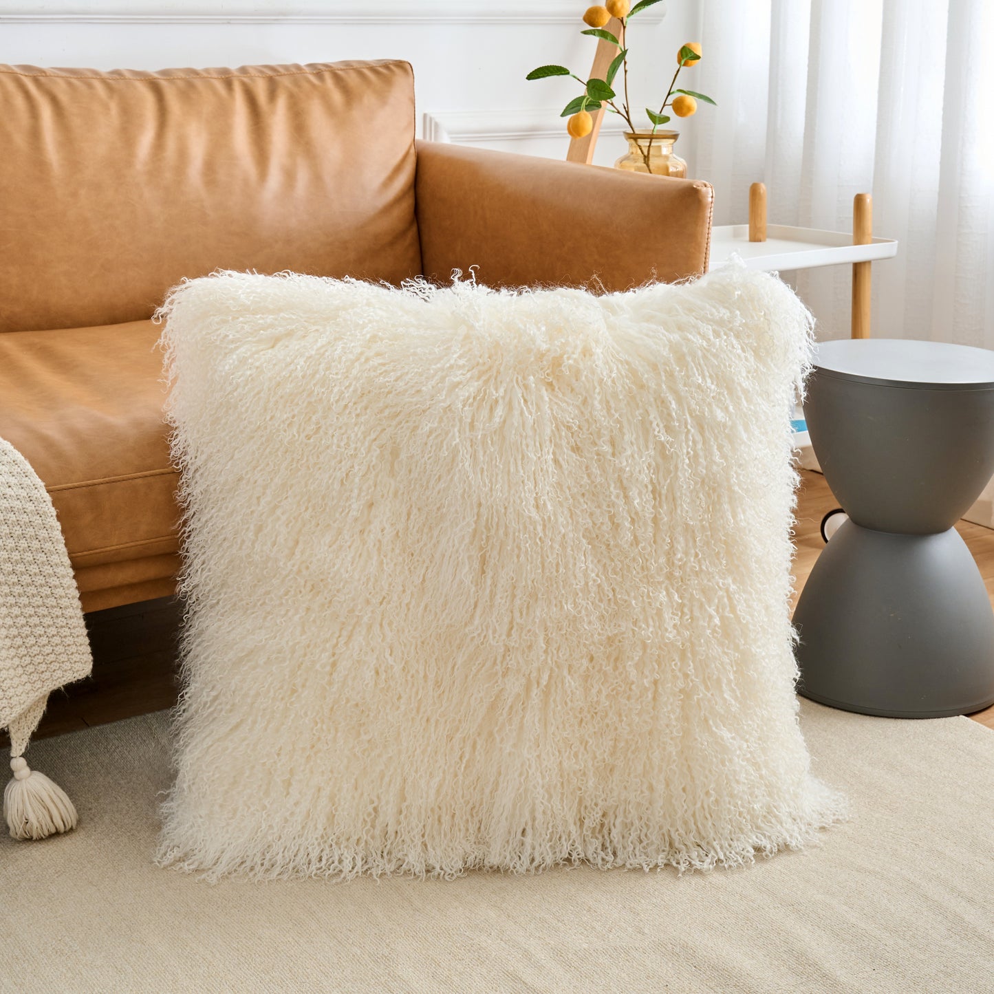 Close-up view of Mongolian lamb fur pillow in natural white on sofa showing soft fluffy curly wool texture in modern interior